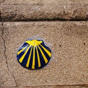 Una concha de vieira de cerámica azul y amarilla, símbolo del Camino de Santiago, está fijada a una áspera pared de piedra.