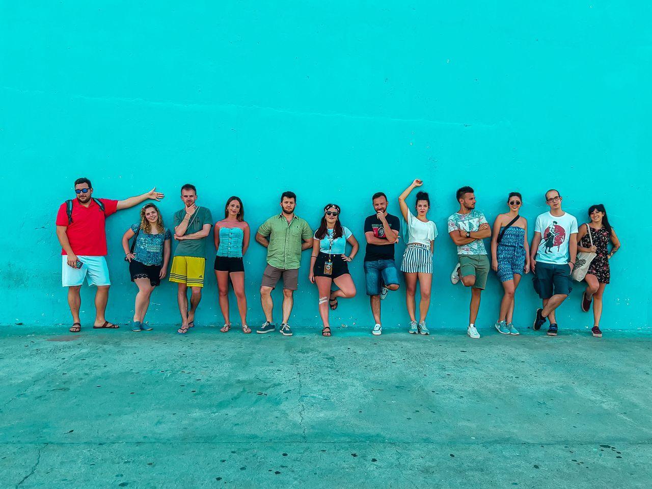 Un grupo de WeRoad posando en fila frente a una pared turquesa sólida sobre un pavimento de hormigón.