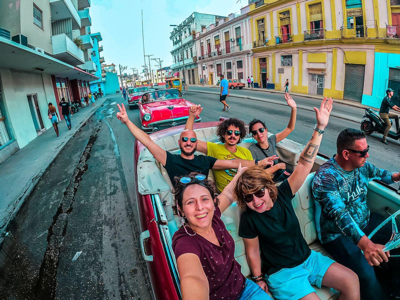 Un groupe WeRoad sourit pour un selfie à bord d'une décapotable rouge classique dans une rue de la ville.