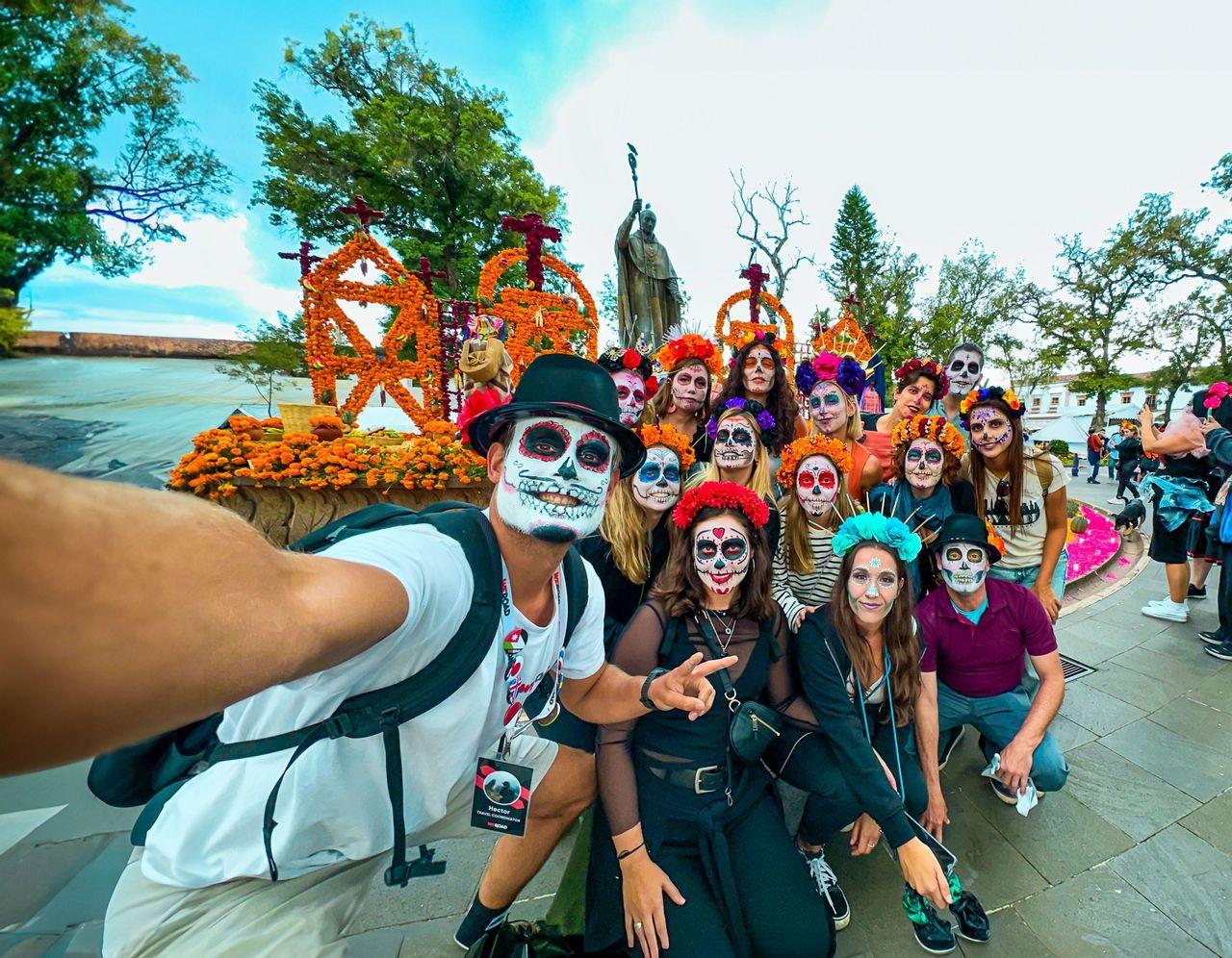 A WeRoad group trip poses for a selfie, all with faces painted as sugar skulls in front of marigold decorations.