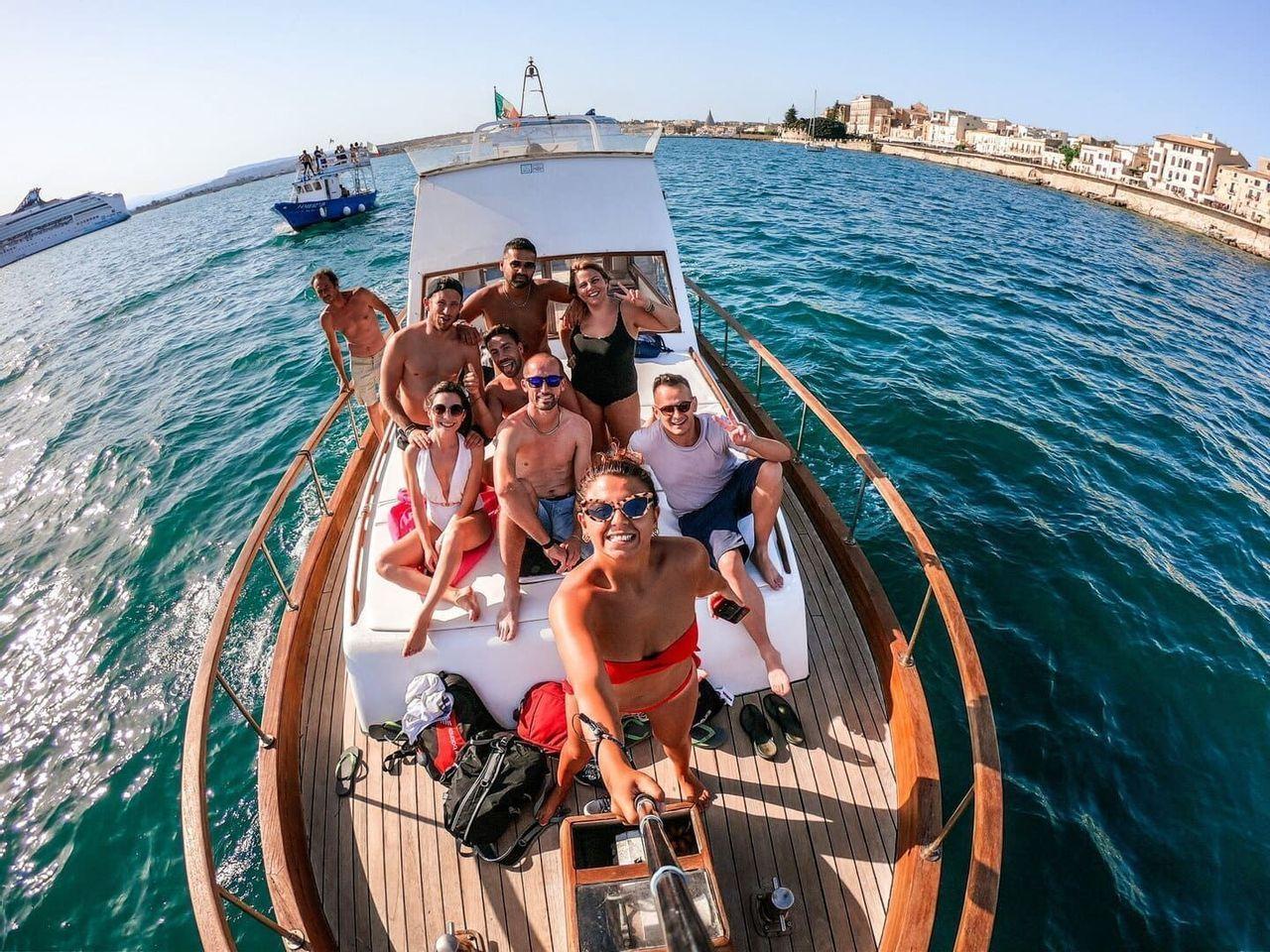 Eine WeRoad-Gruppe macht ein Selfie an Deck eines Holzbootes, das nahe einer Küste auf dem Meer segelt.