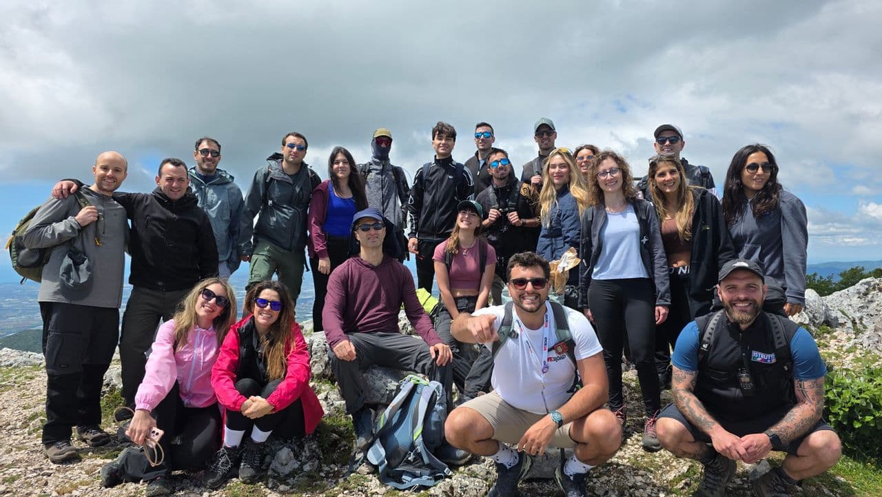 Un gruppo WeRoad in viaggio posa per una foto di gruppo su una vetta rocciosa di montagna sotto un cielo nuvoloso.