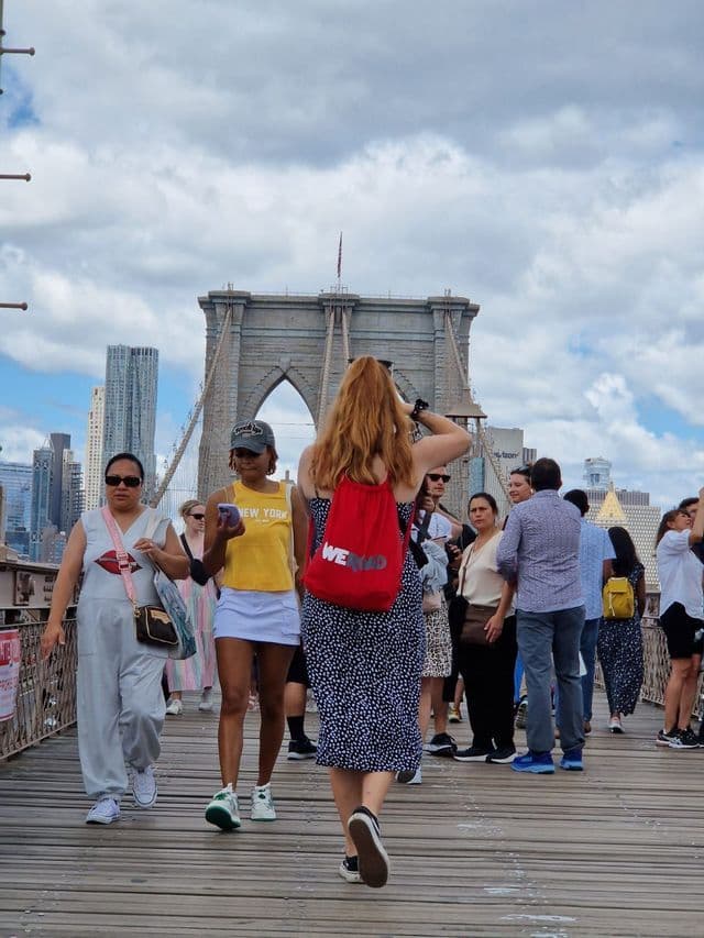 Un gruppo WeRoad cammina su un ponte di legno affollato verso una grande torre di pietra con lo skyline di una città sullo sfondo.