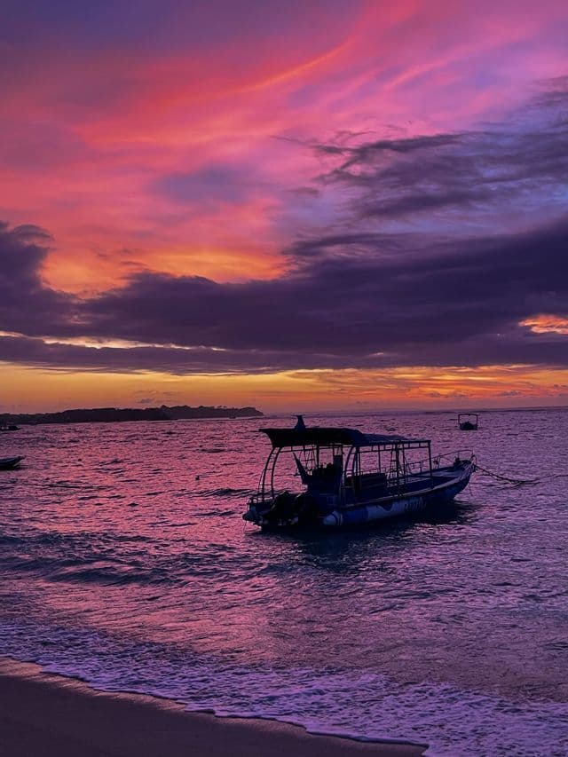 Una barca ancorata nel mare riflette i colori vivaci rosa e viola del cielo al tramonto.