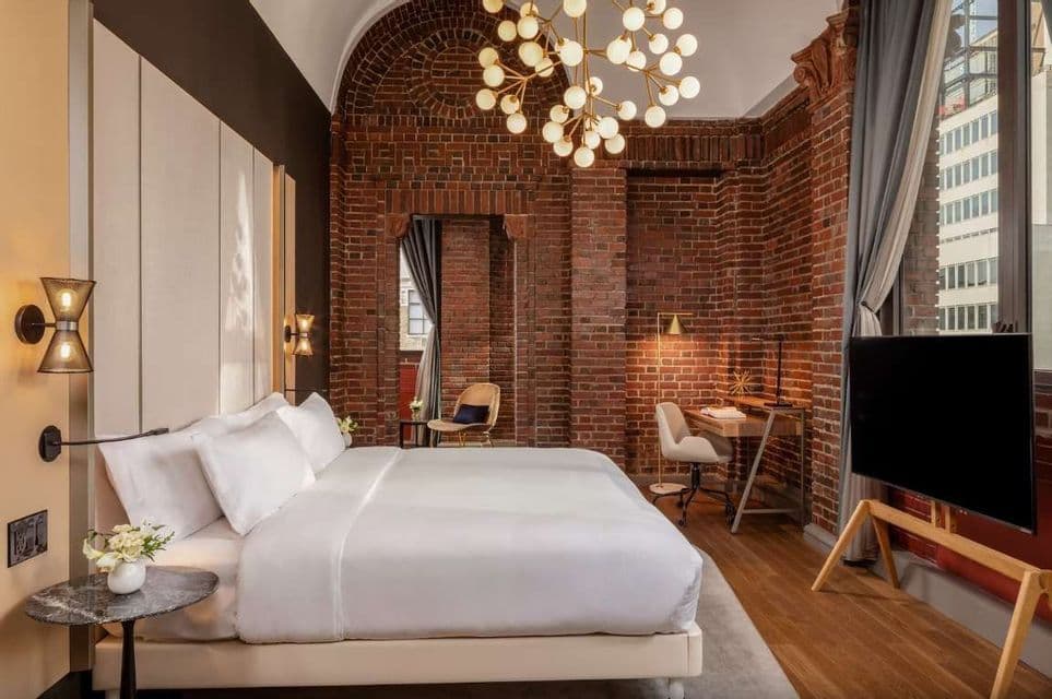 Una camera d'albergo moderna con pareti in mattoni rossi a vista, un grande letto con lenzuola bianche e un lampadario a globo contemporaneo.