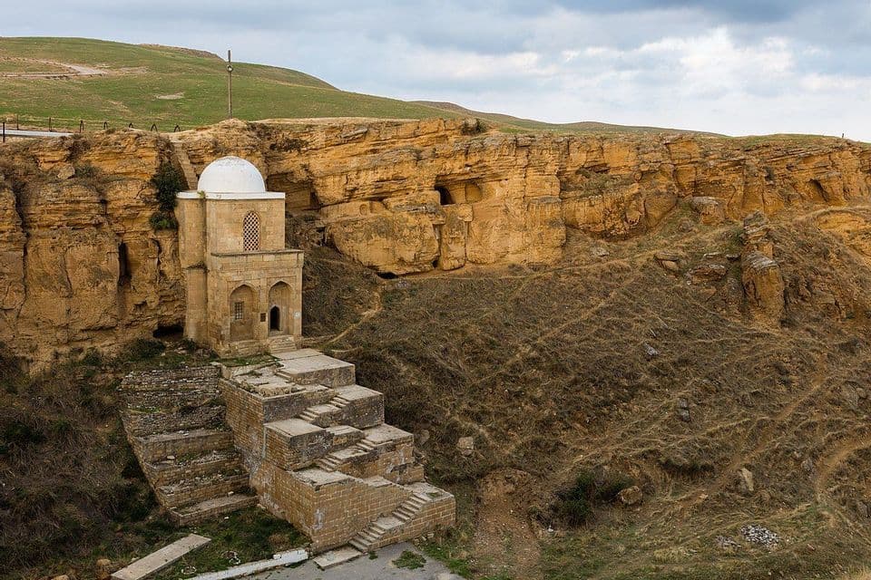 Un mausoleo di pietra con cupola bianca incastonato in una scogliera rocciosa, con ampie piattaforme e gradini in pietra in primo piano.