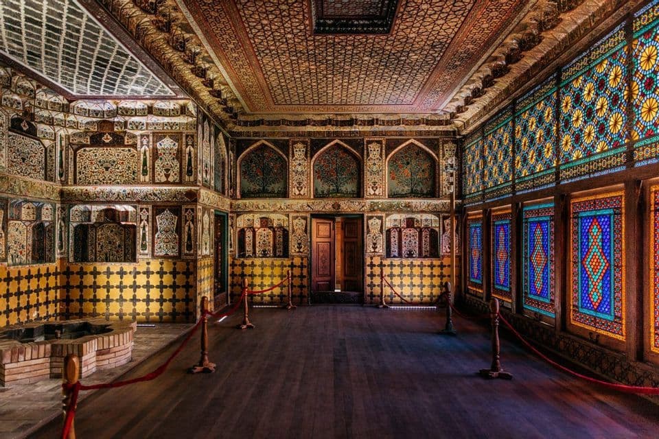 L'interno vuoto di una sontuosa sala con intricati mosaici, un soffitto a motivi e vetrate colorate.