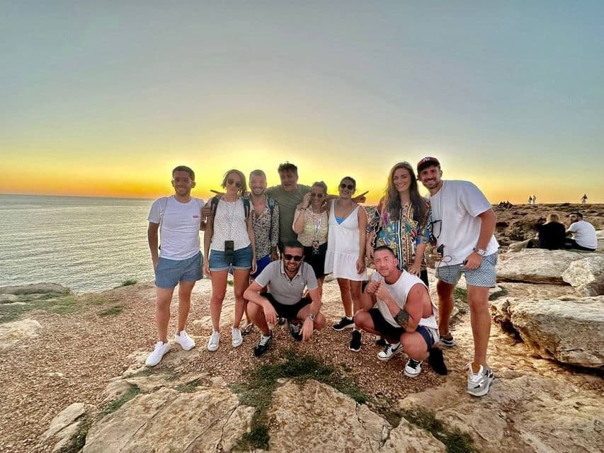 Un grupo de WeRoad posa para una foto en un acantilado rocoso con vistas al mar durante un atardecer dorado.
