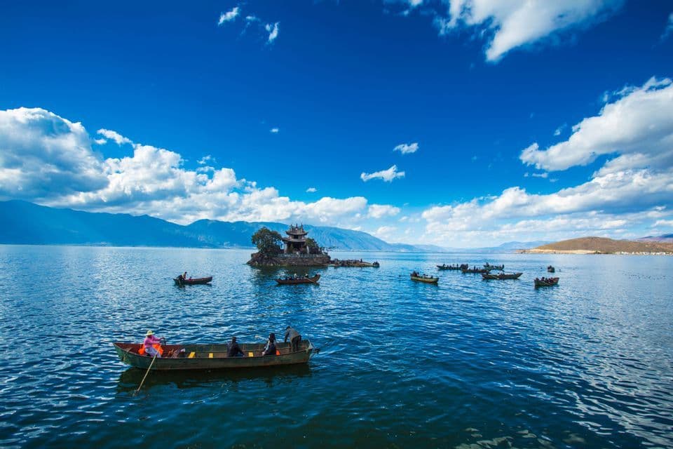Un viaje en grupo de WeRoad navega en pequeñas embarcaciones por un vasto lago azul que rodea una diminuta isla con un templo tradicional.