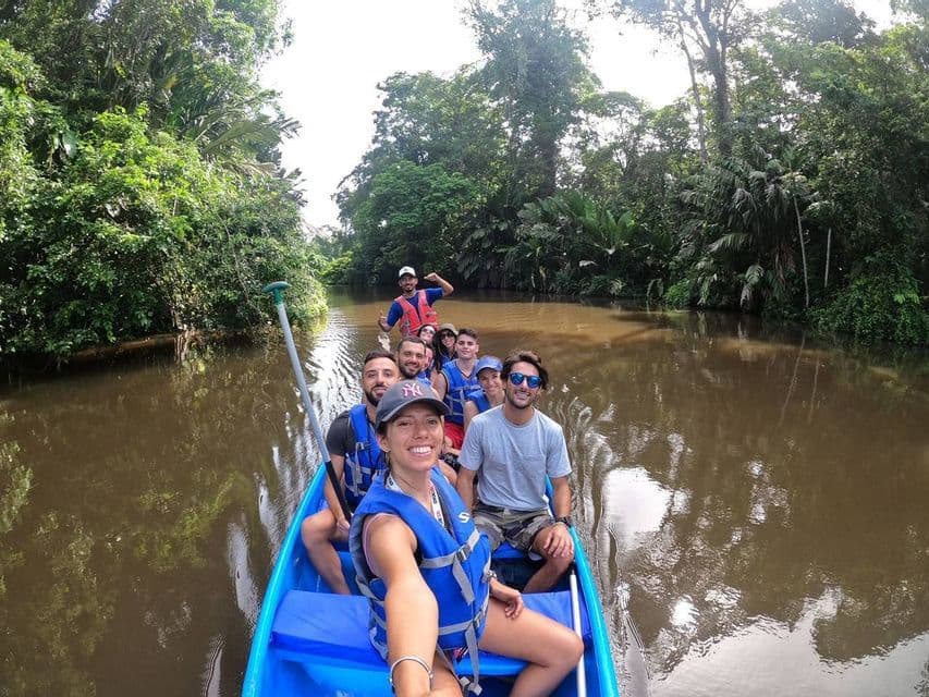 Un grupo de WeRoad con chalecos salvavidas se toma una selfie mientras navega en una canoa azul por un río a través de una densa selva.