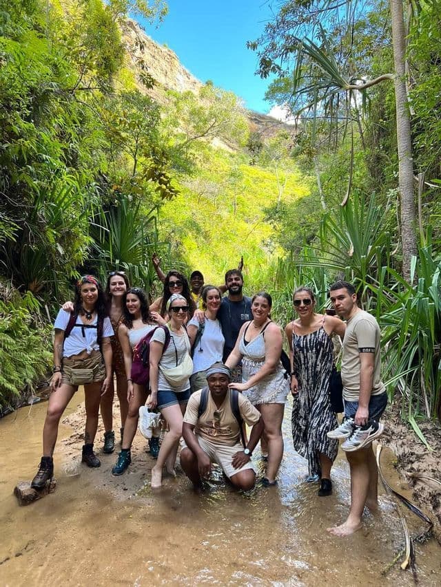 Un grupo de WeRoad posa para una foto en un arroyo poco profundo, en medio de una selva exuberante y verde.