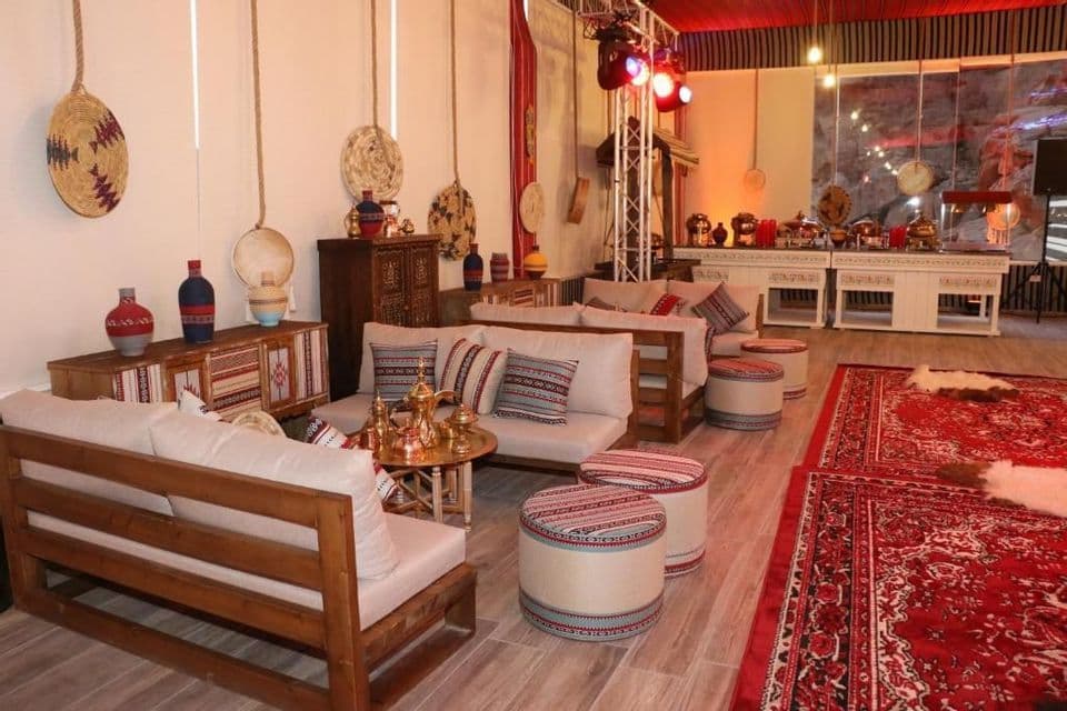 Un'area lounge arredata in stile tradizionale con mobili in legno, cuscini fantasia, tappeti rossi e un buffet sullo sfondo.