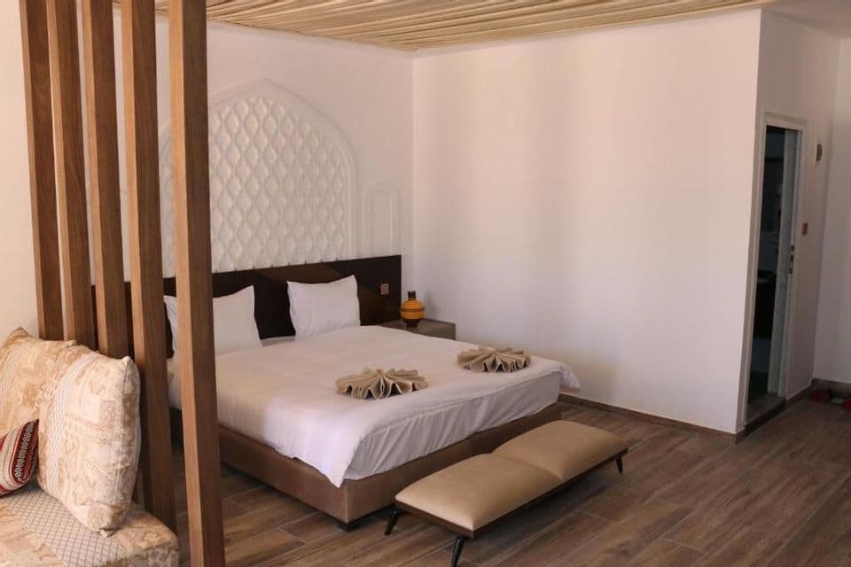 Ein Hotelzimmer mit einem Doppelbett, einem weißen gesteppten Kopfteil und einem hölzernen Raumteiler neben einem gemusterten Sofa.