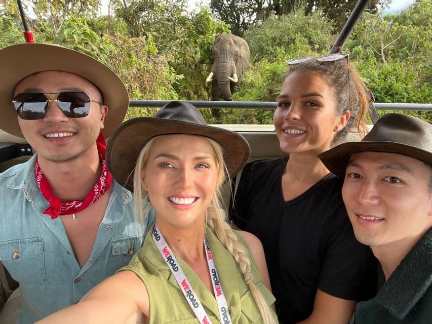 Eine WeRoad-Gruppe macht ein Selfie in einem Safari-Fahrzeug mit einem Elefanten im Dschungelhintergrund.