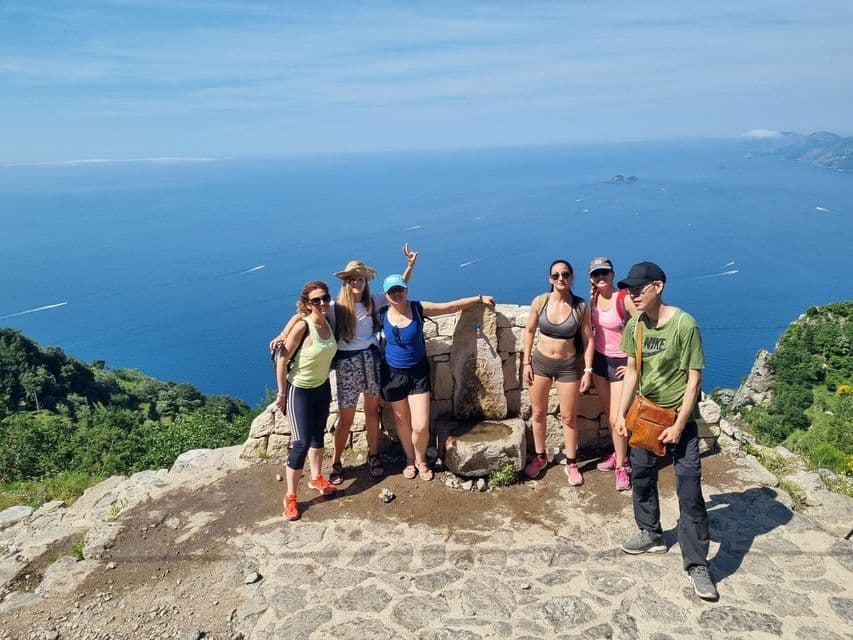 Un viaggio di gruppo WeRoad di sei persone in posa per una foto su un punto panoramico sulla scogliera che si affaccia su un vasto mare blu in una giornata di sole.
