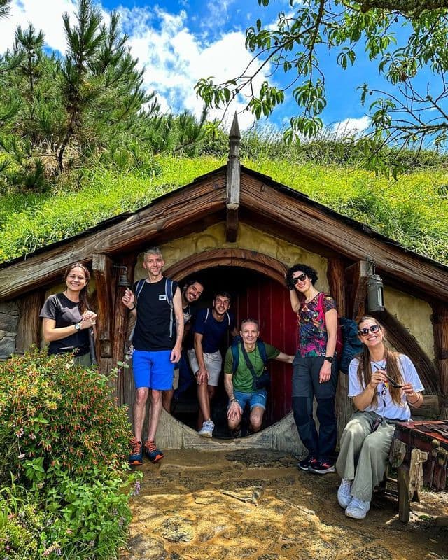 Un viaggio di gruppo WeRoad con sette persone in posa davanti a una casa con porta rotonda, incastonata in una collina erbosa.