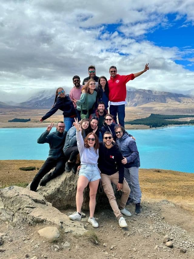 Un gruppo WeRoad in posa su uno sperone roccioso, con vista su un lago turchese e montagne lontane.