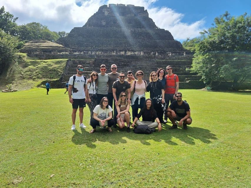Un viaggio di gruppo WeRoad posa per una foto su un prato verde di fronte a un'antica piramide a gradoni in pietra.