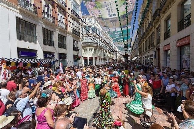 Donne in colorati abiti da flamenco ballano in una strada gremita di persone durante un festival cittadino.