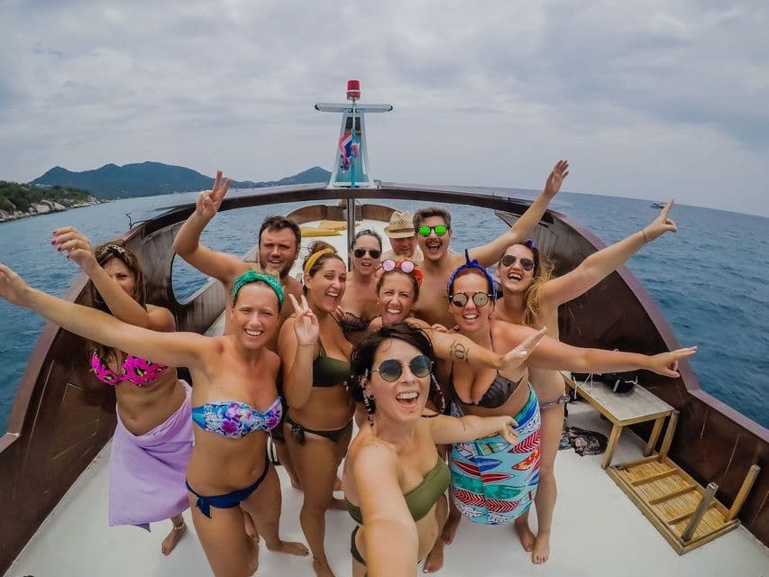 A WeRoad group trip of people in swimwear posing for a selfie on the deck of a boat at sea.