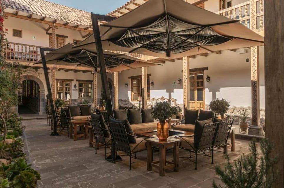 Un patio esterno con sedie a sdraio, divani e grandi ombrelloni allestito nel cortile di un edificio tradizionale.