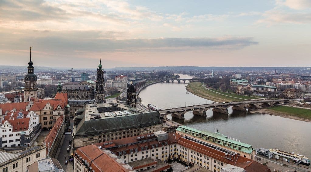 An aerial view of a historic European city with a wide river, several stone bridges, and ornate architecture under a cloudy sky.