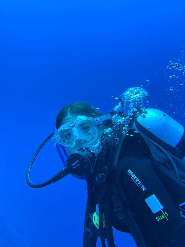 Una toma de primer plano de un buzo con máscara y regulador, flotando bajo el agua en aguas azul profundo con burbujas ascendiendo.