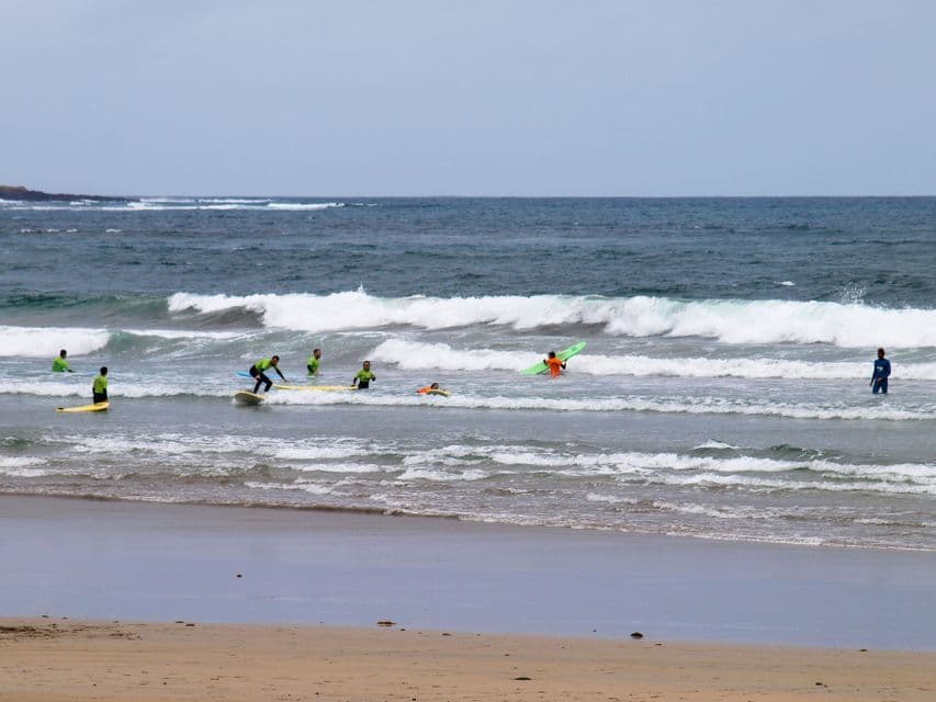Un viaggio di gruppo WeRoad con una lezione di surf nell'oceano, tra onde piccole e un cielo nuvoloso.