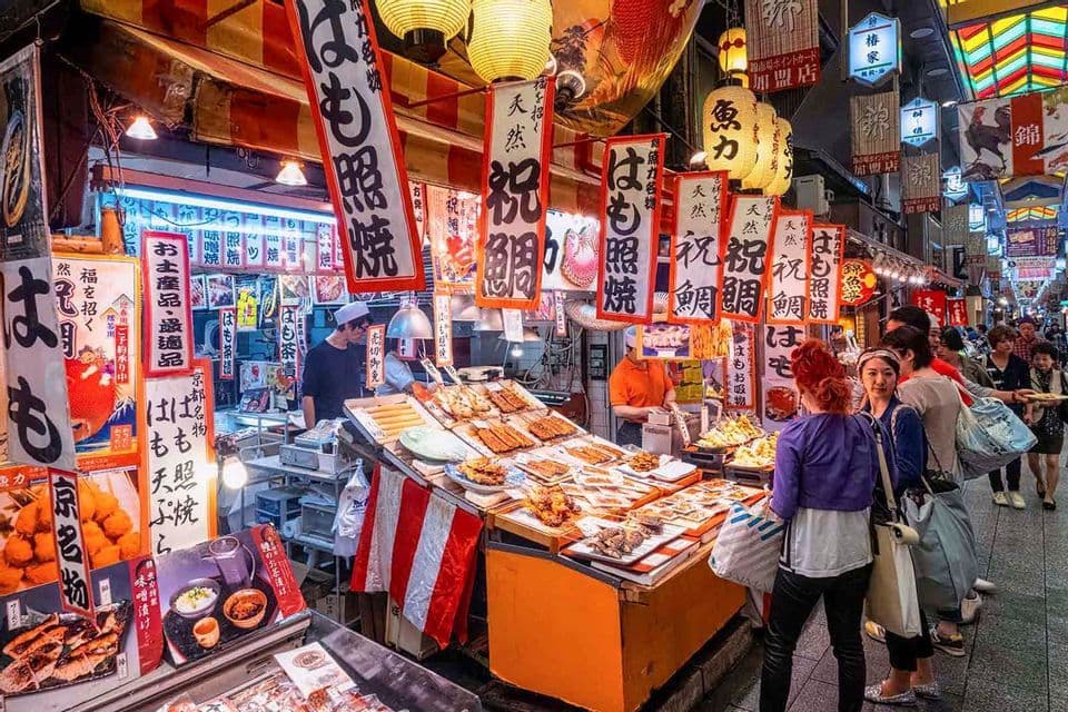 Kunden stöbern an einem Essensstand, der gegrillte Meeresfrüchte auf einem geschäftigen japanischen Markt mit Papierlaternen verkauft.