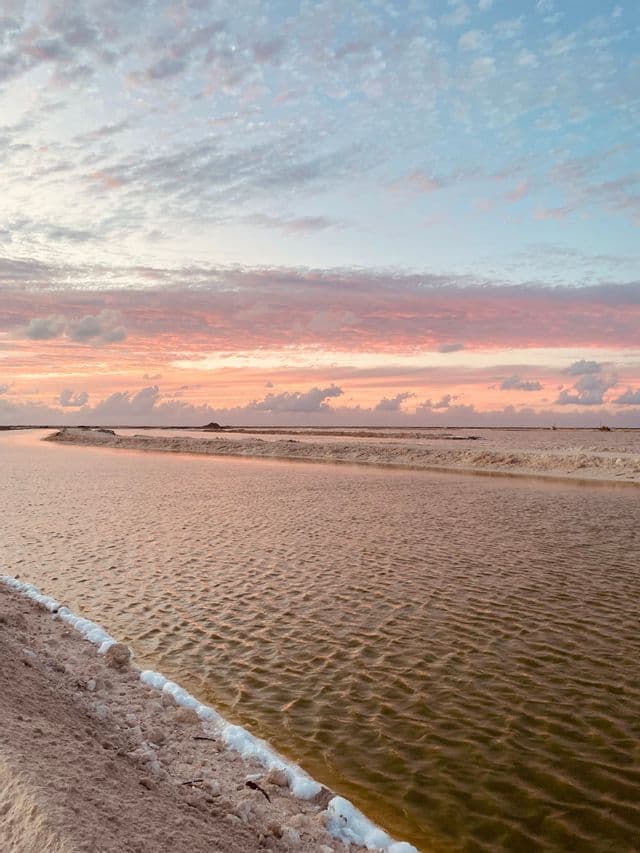Salines avec des canaux d'eau reflétant un ciel de coucher de soleil coloré avec des nuages roses et bleus.
