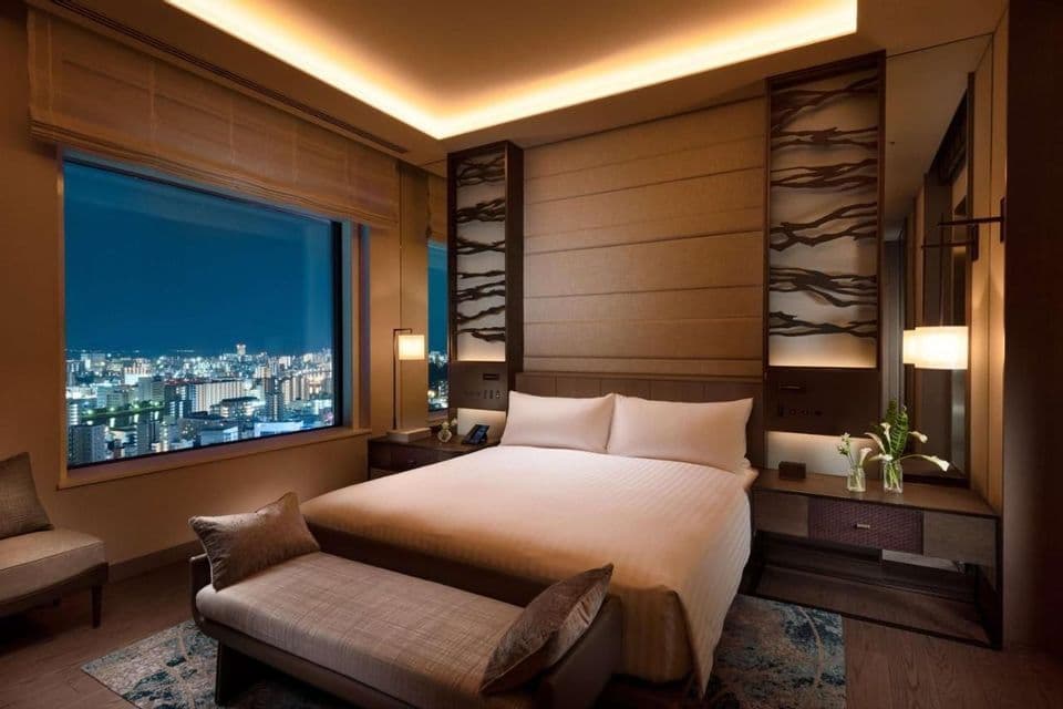 Une chambre d'hôtel moderne avec un grand lit, un éclairage d'ambiance et une vue sur la ligne d'horizon de la ville la nuit.