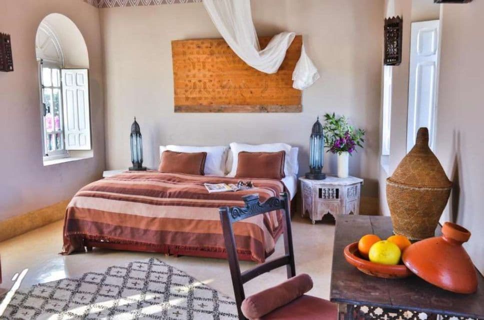 Una camera da letto in stile marocchino, caratterizzata da un letto con coperta a righe, lampade ornate e un tavolo con una pentola tagine.