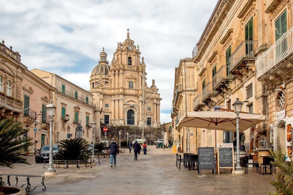 La gente camina por una amplia plaza pavimentada hacia una ornamentada catedral barroca con una gran cúpula.