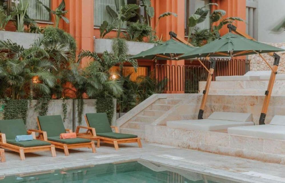 Chaises longues et parasols installés près d'une piscine dans un complexe hôtelier avec des plantes luxuriantes et un bâtiment en terre cuite.