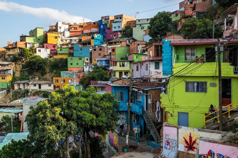 Un quartier dense de maisons aux couleurs vives construites sur une colline verdoyante sous un ciel partiellement nuageux.
