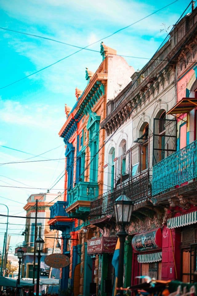 Una vista en contrapicado de una calle bordeada de edificios históricos y coloridos, con balcones ornamentados, bajo un cielo azul claro.