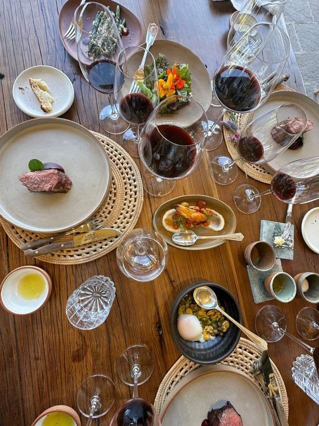 Una mesa de madera vista desde arriba, con varios platos gourmet y copas de vino tinto para un maridaje.