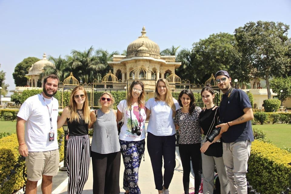 Un viaje en grupo de WeRoad con ocho personas posando juntas en un jardín soleado frente a un edificio ornamentado y abovedado con palmeras.