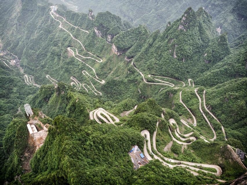 Una vista aerea di una lunga strada tortuosa con molti tornanti che sale su una catena montuosa ripida e verde.