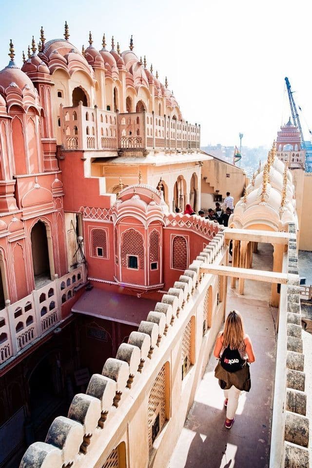A woman on a WeRoad group trip walks on a high terrace, looking out over ornate pink and peach-colored architecture.