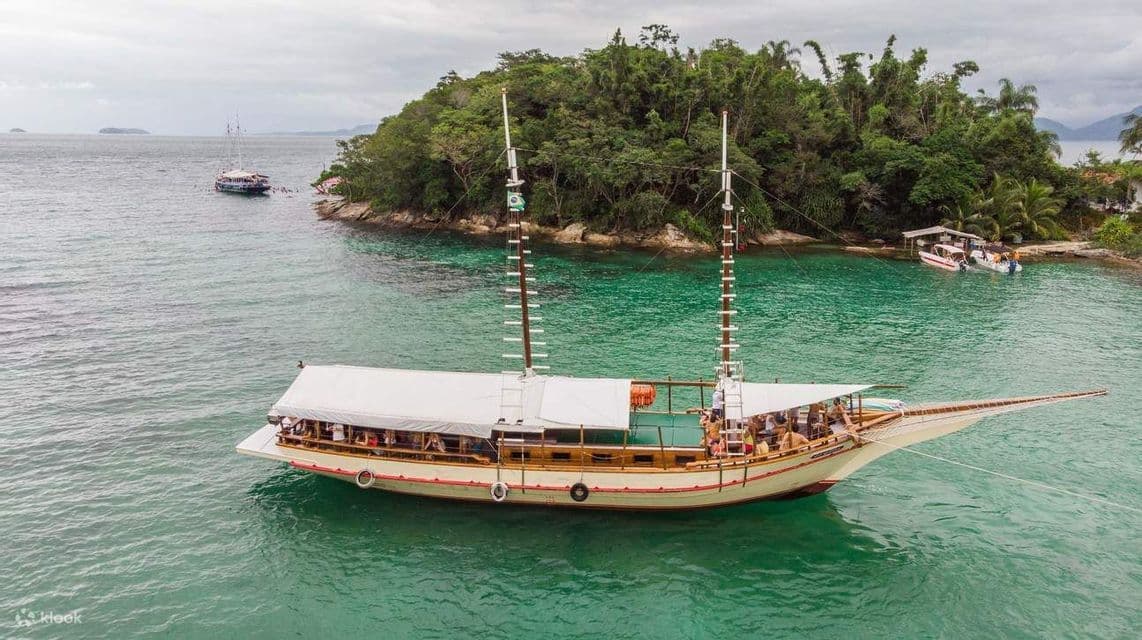 Un viaggio di gruppo WeRoad su una goletta che galleggia su acque turchesi accanto a un'isola lussureggiante e alberata.