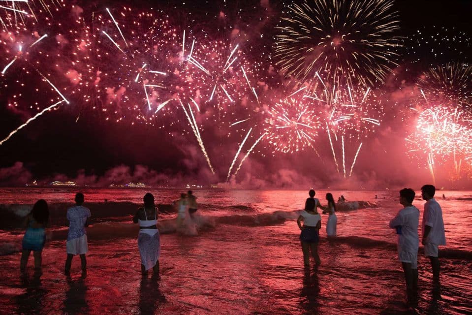 Un gruppo WeRoad in viaggio di notte in mare osserva fuochi d'artificio rossi che esplodono nel cielo.