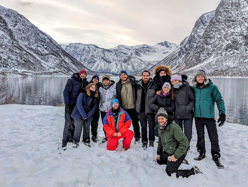 Un grupo de viaje de WeRoad sonríe para una foto en un paisaje nevado, con un fiordo y montañas al fondo.