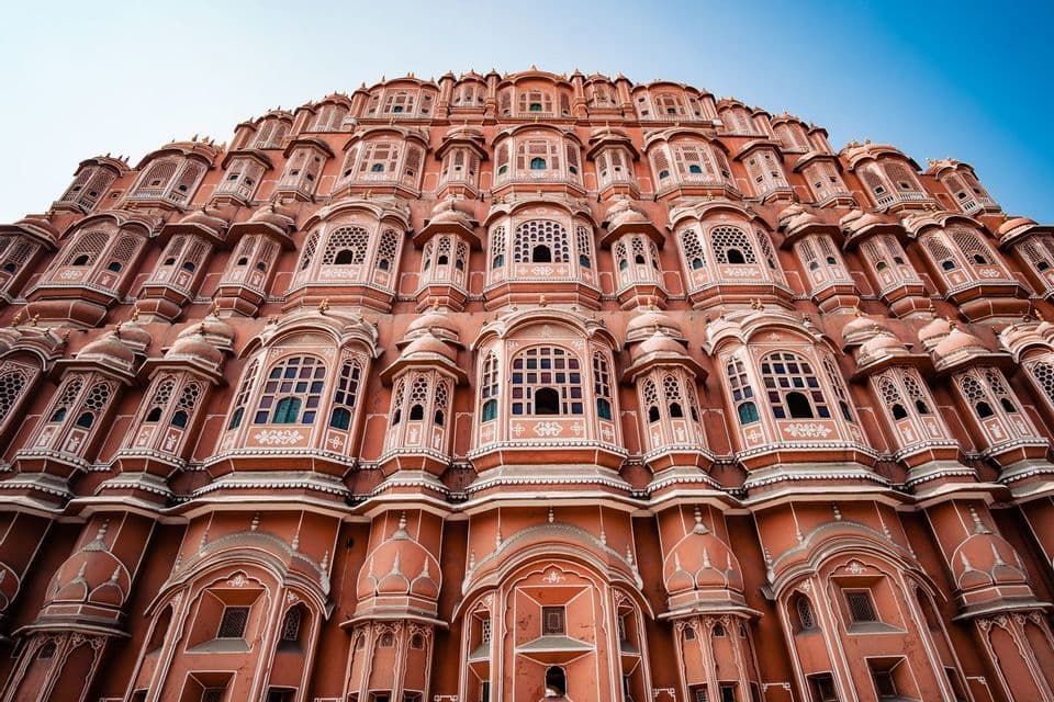 Vista en contrapicado de la ornamentada fachada rosa de varias plantas de un palacio con intrincadas ventanas, bajo un cielo azul claro.