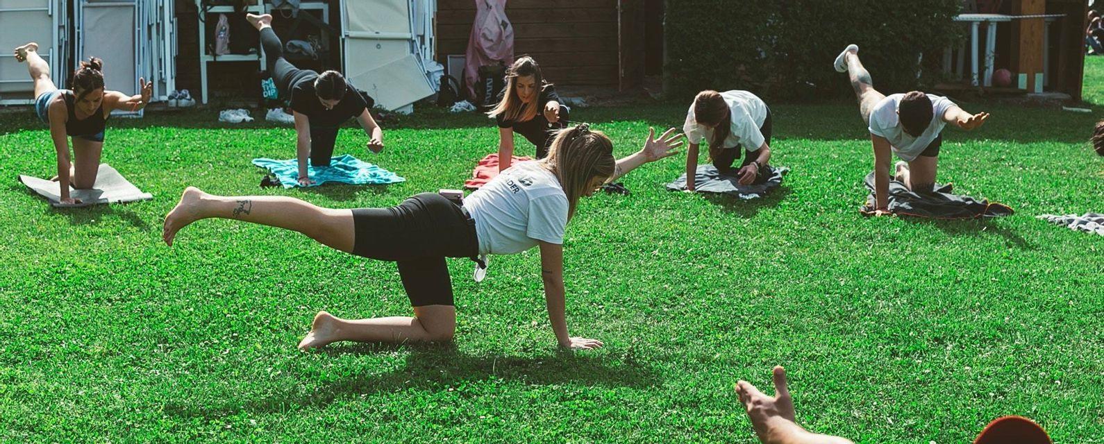Un viaggio di gruppo WeRoad mentre pratica una posa yoga di equilibrio su un prato verde brillante.