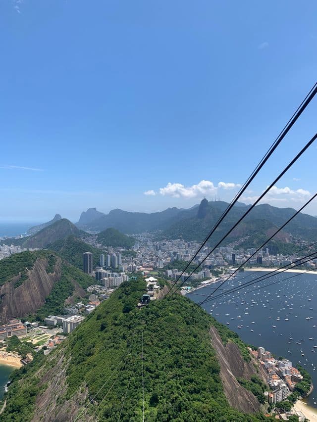 Una vista dall'alto da una funivia che guarda una città costiera circondata da montagne verdi e una baia con molte barche.