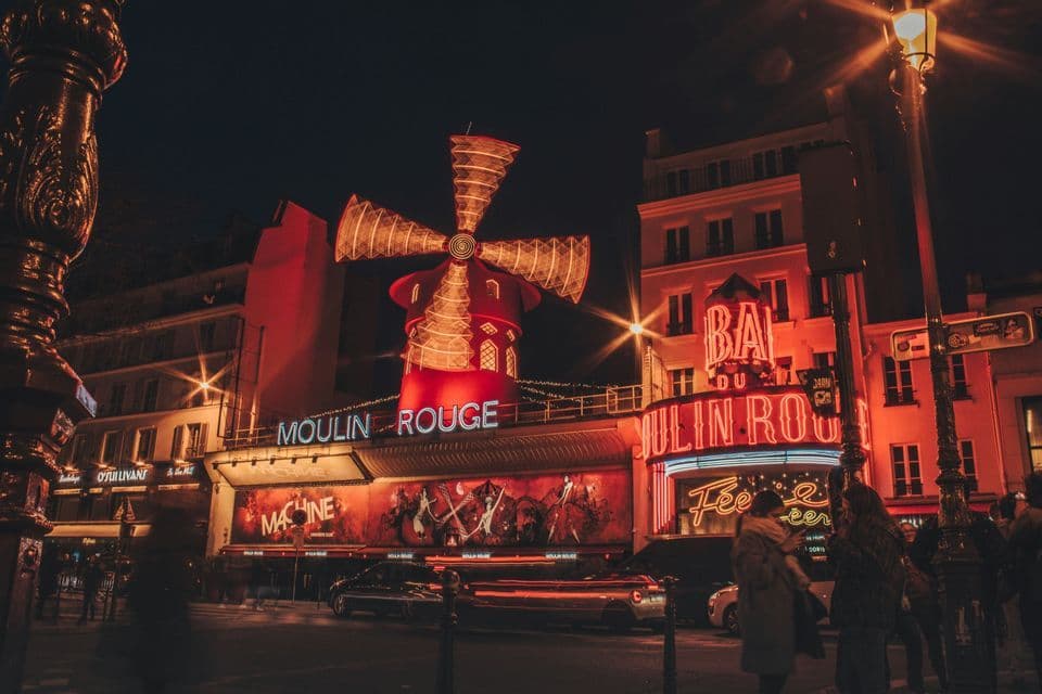Das Moulin Rouge Gebäude bei Nacht, mit seiner ikonischen roten Windmühle und hell erleuchteten Neonschildern über einer belebten Straße.
