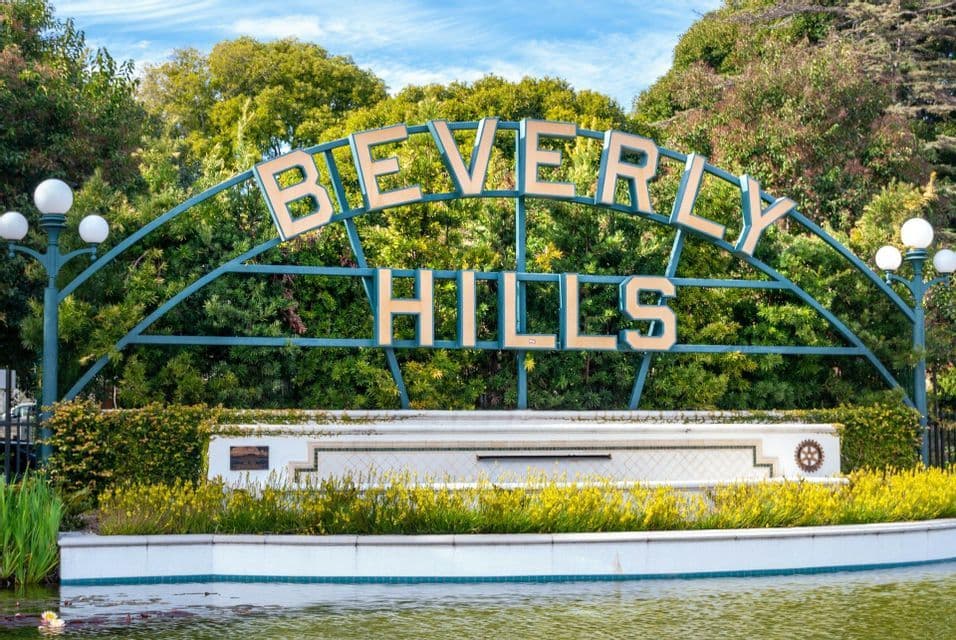 L'iconica insegna di Beverly Hills si trova in un parco con un laghetto in primo piano e alberi verdi lussureggianti sotto un cielo blu.