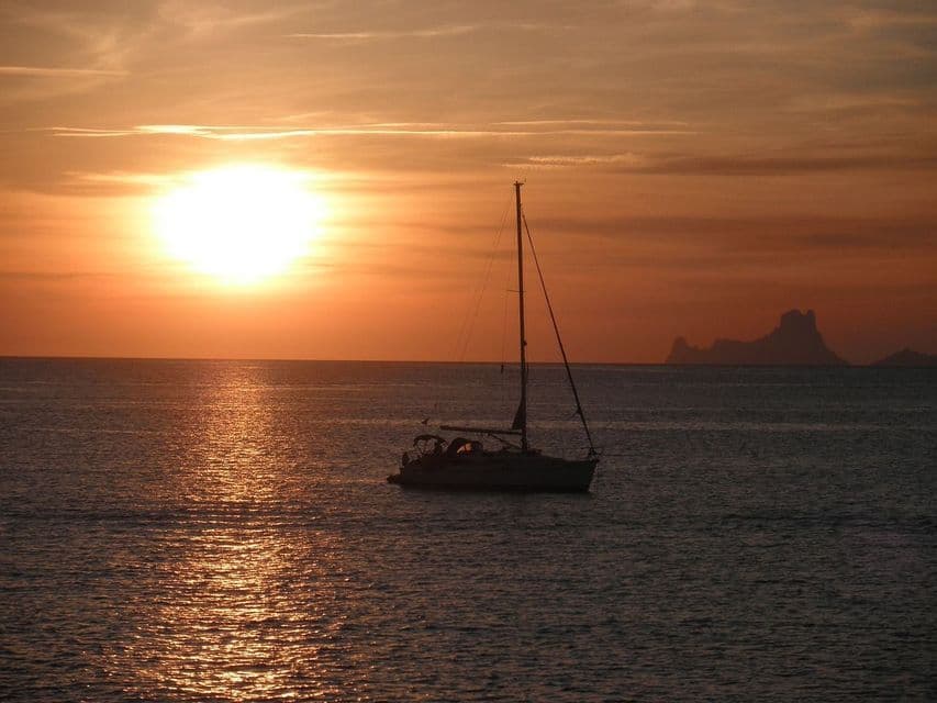Un velero se recorta en el océano durante un atardecer dorado, con una isla distante en el horizonte.