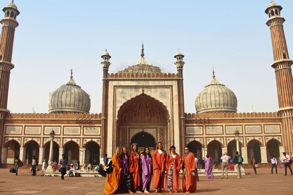 A WeRoad group trip wearing colorful robes stands together for a photo in front of a large mosque with domes and minarets.